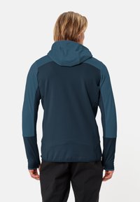 Giacca tecnica blu con cappuccio, dotata di un tessuto testurizzato, pannelli di colore a contrasto e vestibilità aderente. Adatta per attività all'aperto.