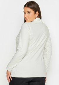 Vit långärmad topp med design av en hög krage, mjukt tyg, figurnära passform och sömlösa axlar, tillsammans med svarta byxor.