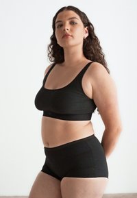 Black cotton bra with wide straps, paired with matching high-waisted briefs. Smooth texture and minimalistic design.