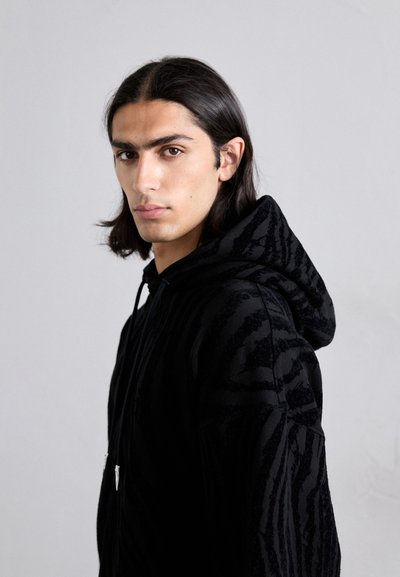 Hanorac negru cu un model texturat de dungi de tigru. Design cu glugă, cu șnururi și detalii cu fermoar argintiu în față.