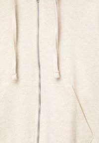 Helle beige Zip-Hoodie aus weichem Baumwollmaterial. Verfügt über eine Fronttasche und Kordeln mit strukturierten Enden.