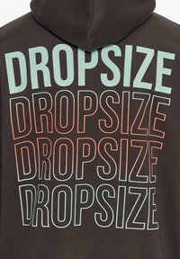 Mørk hættetrøje med gentaget tekst "DROPSIZE" i varierende skrifttyper; farverne skifter fra teal til koral. Blød, blanding af bomuld og tekstil.