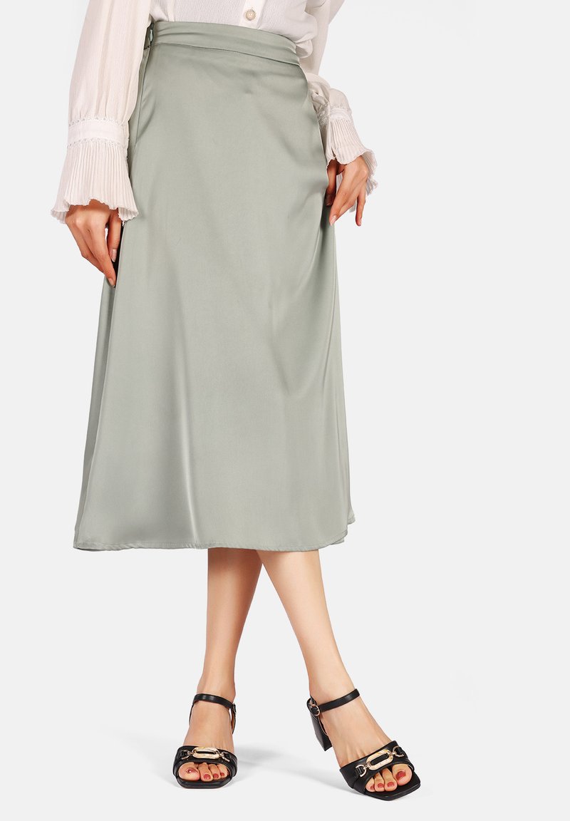 Gonna midi in satin verde chiaro con una texture liscia. Abbinata a sandali neri con un elegante dettaglio dorato a forma di fibbia.