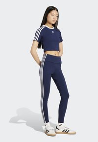 Tamno plava sportska kratka majica s bijelim detaljima, uparena s tamnoplavim tajicama koje imaju bijele bočne pruge. Model nosi klasične tenisice.