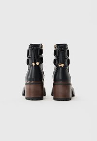 Pair of black leather ankle boots with chunky brown stacked heels and gold-accented laces at the back on a white background.