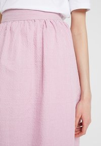 Jupe à rayures roses et blanches avec une taille froncée, présentant une texture lisse et un tissu léger qui tombe sous le genou.