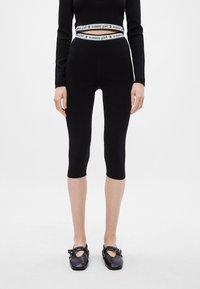 Crne tajice s visokim pojasom koje sadrže bijeli logo "tommy girl". Glatka tkanina i kroj do koljena, upotpunjene crnim ravnim cipelama.