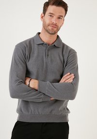 Grijze polo met lange mouwen en een geribde kraag, drie-knopen sluiting en elastische manchetten. Voorzien van een zachte, gestructureerde stof.