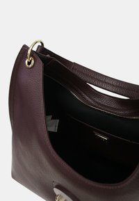 Sac à main en cuir bordeaux avec une finition texturée, quincaillerie dorée, bandoulière unique et un haut ouvert révélant un intérieur noir et une poche zippée.