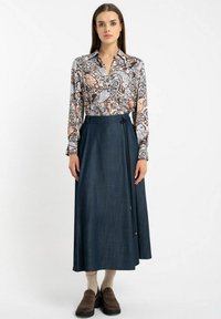 Bluzka z długim rękawem w wielokolorowy kwiatowy wzór połączona z ciemnoniebieską spódnicą w formie owijanej, z wiązaniem w talii i długości do kostek. Brązowe obuwie.