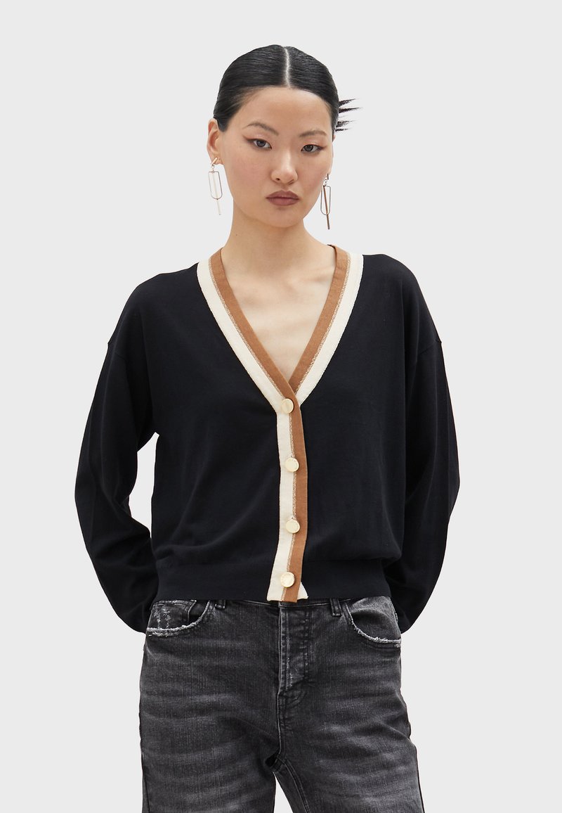 Black cardigan with a deep V-neck, cream and brown accents, five cream buttons down the front, and relaxed fit sleeves.