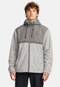 Hooded zip-up jacket in light grey and darker grey. Features a textured yoke, black accent stitching, and side pockets. Soft fabric.