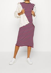 Mittel langes, gestreiftes Kleid in Marineblau, Rot und Weiß mit kurzen Ärmeln, kombiniert mit einer cremefarbenen, oversized Jacke und weißen Sneakers.