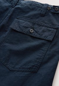 Temno modre hlače z teksturirano tkanino, enojnim žepom s poklopcem in zapenjanjem z gumbom ter dvema gumboma na pasu.