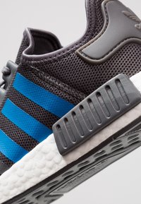 Svart mesh-sneaker med blå randiga detaljer, grå hårdvara, en texturerad sula och en vadderad vit mellansula.