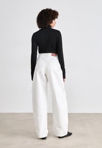 Witte wijde jeans met een hoge taille en achterzakken, gecombineerd met een getailleerde zwarte coltrui. Opvallend leren label bij de taille.