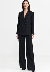 Czarny marynarka podwójnie zapinana z głębokim dekoltem w kształcie litery V, dopasowany krój i szerokie spodnie. Gładki materiał bez widocznych wzorów lub ozdób.