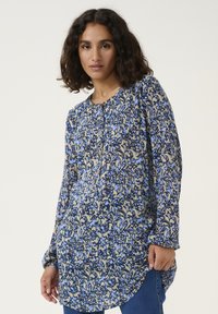 Blouse à manches longues en motif floral bleu et beige, encolure ronde avec boutons, tissu doux, ourlet courbé, coupe décontractée.