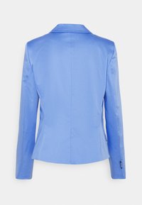 Blazer bleu clair sur mesure avec une texture lisse, manches longues et col à revers cranté. Présente une silhouette cintrée et des détails de coutures à l'arrière.