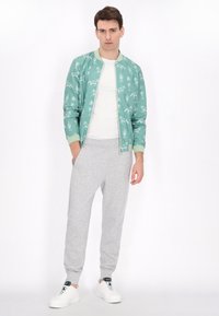 Mintgroene bomberjack met witte dierenprint, gecombineerd met lichtgrijze sweatpants en witte sneakers. Eenvoudig, casual ontwerp.