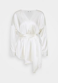 Vit satinwrap-topp med långa ärmar, V-ringning och ett knytbälte i midjan. Slät textur med ett flödande mönster och asymmetrisk fåll.