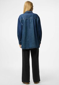 Camicia in denim blu scuro con una vestibilità comoda, dotata di colletto e polsini con bottoni, abbinata a pantaloni neri a gamba larga e calzature marroni.