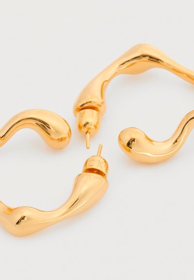 Χρυσόσκονες σκουλαρίκια σε σχήμα βρόχου με λείες, ακανόνιστες κυρτές μορφές και κλείσιμο με καρφί, σε απλό λευκό φόντο.