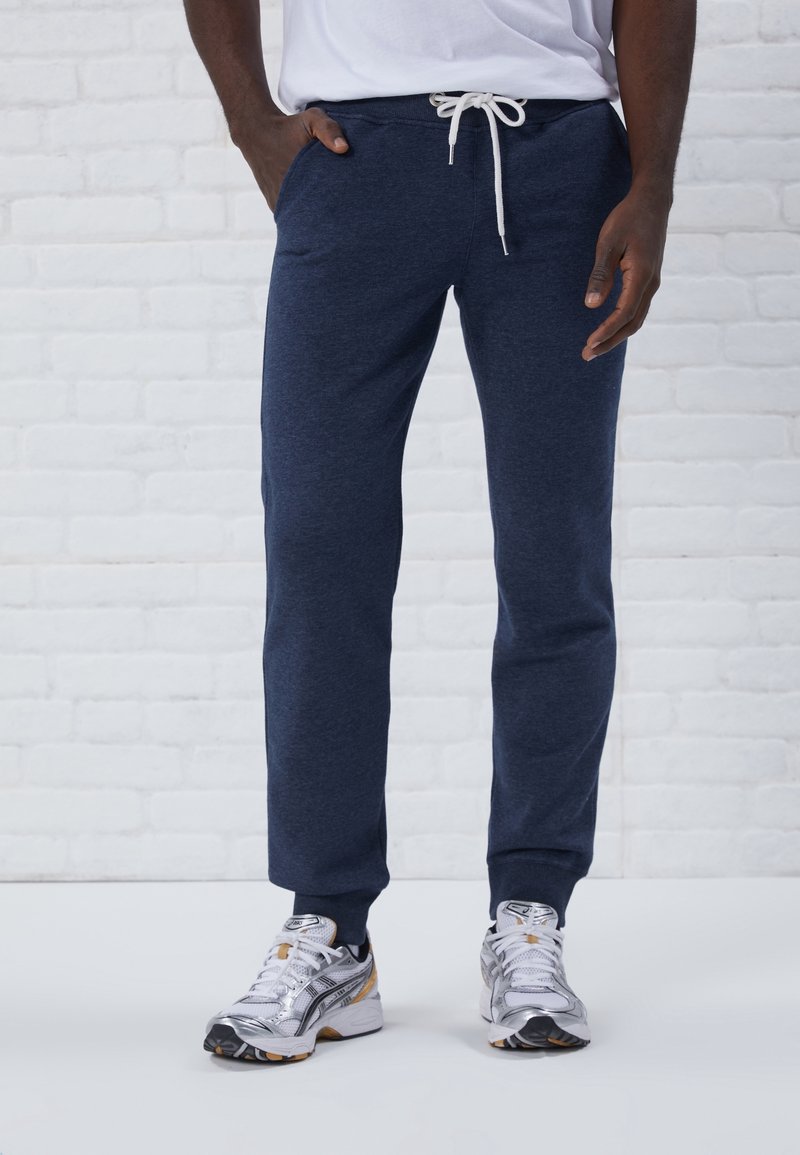 Navyblaue Jogginghose aus weichem Stoff mit Kordelzugbund und Seitentaschen, kombiniert mit silbernen Laufschuhen.