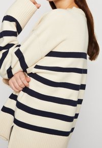 Gebreide trui met horizontale strepen in crème en marineblauw, geribbelde manchetten en een ontspannen pasvorm. Gestructureerde stof met zijsplits aan de zoom.