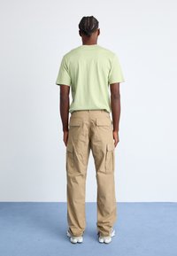 Hellgrünes T-Shirt mit kurzen Ärmeln und lockerer Passform, kombiniert mit beigen Cargo-Hosen, die Seitentaschen und ein gewebtes Label haben.