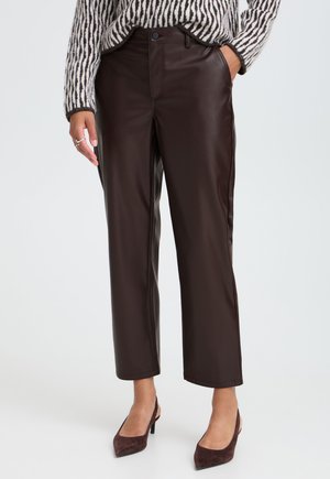 Femme portant un pantalon droit en simili cuir marron foncé, des talons en daim marron et un pull à manches longues à rayures zèbre.