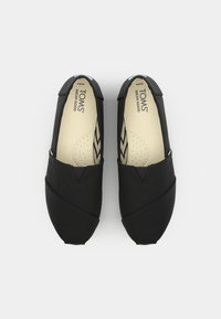 Sorte kanvas slip-on sko med et fleksibelt design, som har en glatt tekstur, sydde detaljer og lystfargede såler med perforeringer.