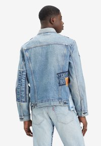 Leren spijkerjack in lichtblauw met patchworkdetails, een klassieke kraag en knoopsluitingen, met verschillende texturen en schaduwen.
