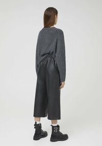 Grau gerippter Pullover, schwarze Kunstleder-Culottes und schwarze Schnürstiefel mit Schnallen, von hinten betrachtet.