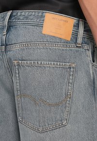 Jasnoniebieskie dżinsy z denimu z skórzan�ą metką na tylnej kieszeni, ozdobione pomarańczowym przeszyciem i zakrzywionym kształtem kieszeni.