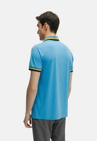 Polo shirt azzurro chiaro con design a tinta unita. Presenta un colletto a contrasto con strisce gialle e blu scuro. Maniche corte, materiale elegante.