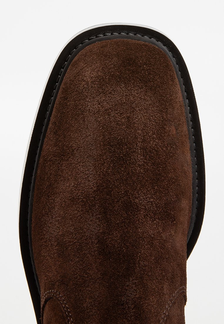 Braune Wildleder-Ankle Boots mit abgerundeter Spitze, schwarzer Gummisohle und detaillierter Naht entlang der Kante. Weiche Textur und glatte Oberfläche.