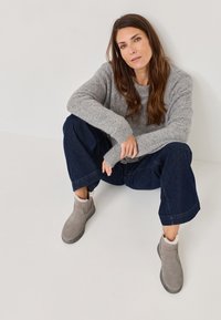 Grijze suède enkellaarsjes met een zachte, gestructureerde voering en rubberen zolen, gecombineerd met een grijze trui en donkere brede jeans.