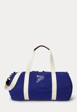 Geantă cilindrică albastră cu bretele albe, accente de mânere din piele maro și logo brodat „Polo 67” pe partea din față.