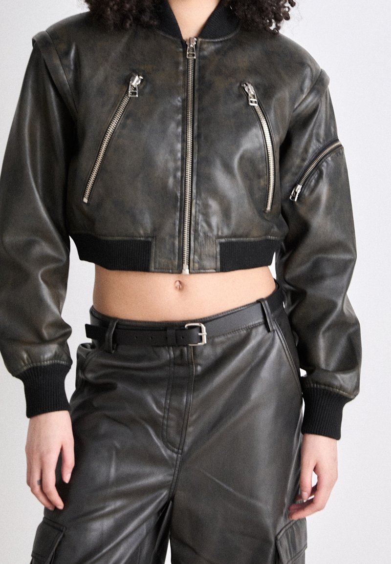 Przycięta kurtka bomberka z ciemnej teksturowanej skóry z srebrnymi zamkami błyskawicznymi, ściągaczami na rękawach i luźnym krojem. W zestawie z dopasowanymi skórzanymi spodniami.