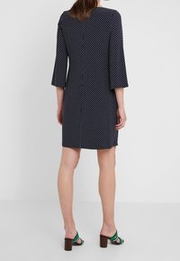 Námořnické šaty s bílými puntíky, tříčtvrteční rozšířené rukávy a kulatým výstřihem. Sahají nad kolena a jsou doplněny zelenými sandály na podpatku.