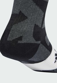 Calcetín negro y gris con un diseño texturizado que presenta una franja blanca y un logo en la parte superior, diseñado para la comodidad y un buen ajuste.