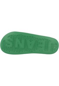Semelle de chaussure en caoutchouc vert avec des motifs de texture pour une adhérence optimale et le mot "JEANS" embossé. Bords légèrement arrondis et design plat.