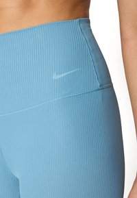Visoke atletske tajice svijetloplave boje, s rebrastom teksturom i suptilnim bijelim Nike logotipom na pojasu.
