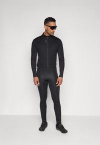 Svart sporty jakke med høy krage, tettsittende svarte leggings og svarte sykkelsko, med en glatt tekstur og minimal merkevare.