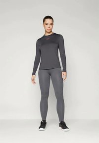 Ciemnoszara, długorękawowa koszulka sportowa o prążkowanej fakturze i czerwonym logo, zestawiona z pasującymi szarymi legginsami o prążkowanej fakturze oraz czarnymi butami sportowymi.