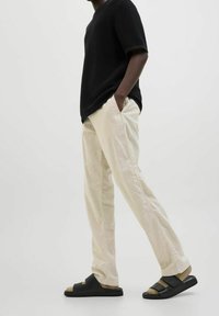 Černá texturovaná košile s krátkým rukávem, béžové volné kalhoty a černé sandály s dvojitým páskem a polstrovanou stélkou.