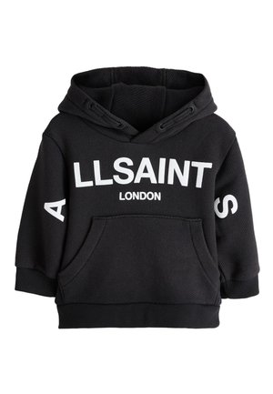 Uśmiechnięte dziecko z warkoczami, ubrane w czarną bluzę z kapturem AllSaints London i czarne spodnie, stojące na tle jednolitego jasnego tła.