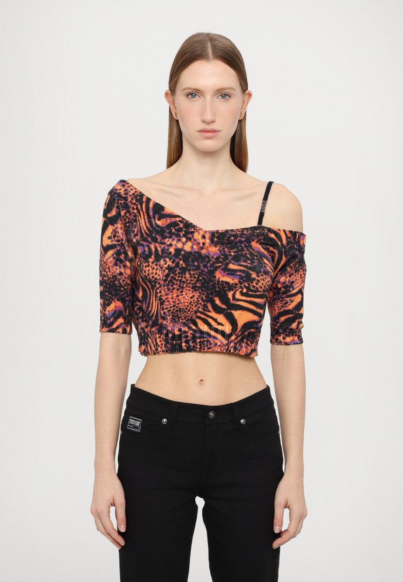 Avkappet off-the-shoulder topp med oransje, svart og lilla dyremønster. Fitted design, ribbet tekstur, korte ermer, kombinert med svarte jeans.