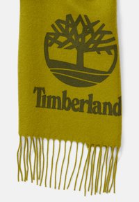 Sciarpa di lana verde con un logo di albero verde scuro e il testo "Timberland", con estremità frangiate e una texture morbida.